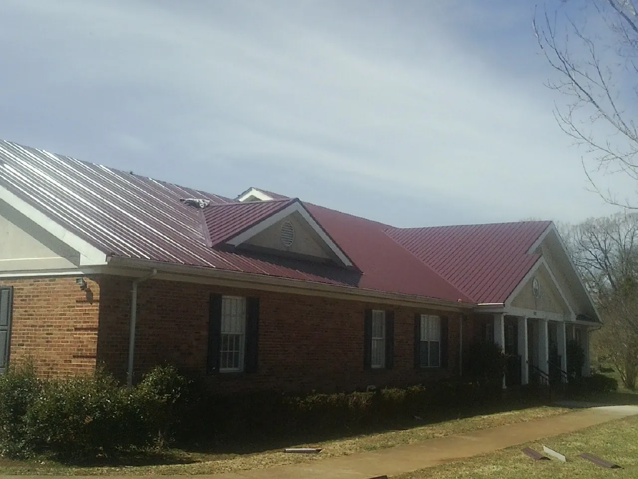 Red metal roof with gabled entries on a long brick building, from a Hail Damage Roof Repair job in Cygnet