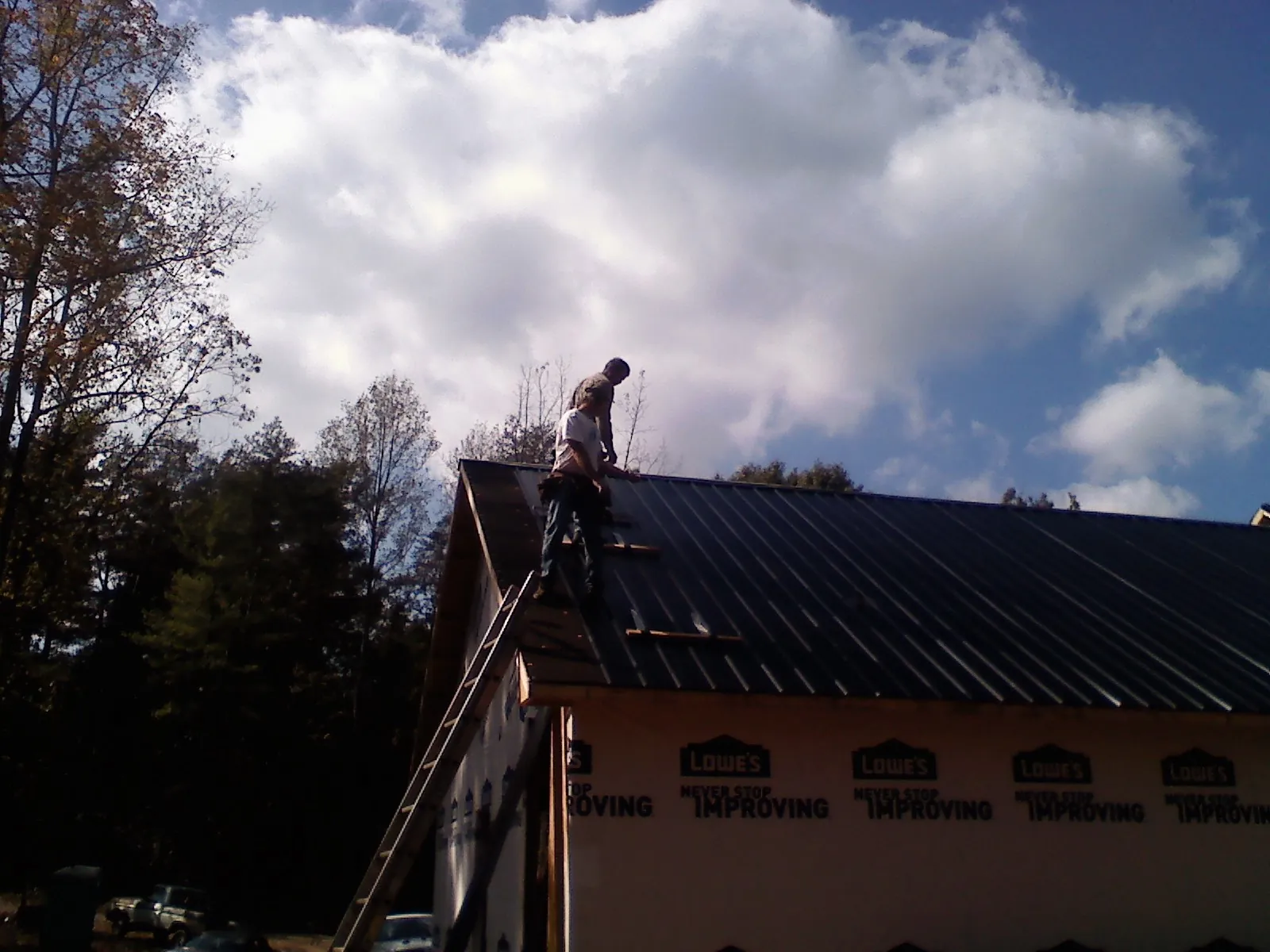 Roofer fastening dark metal panels high against a cloudy sky, from a Roof Inspection job in Cygnet