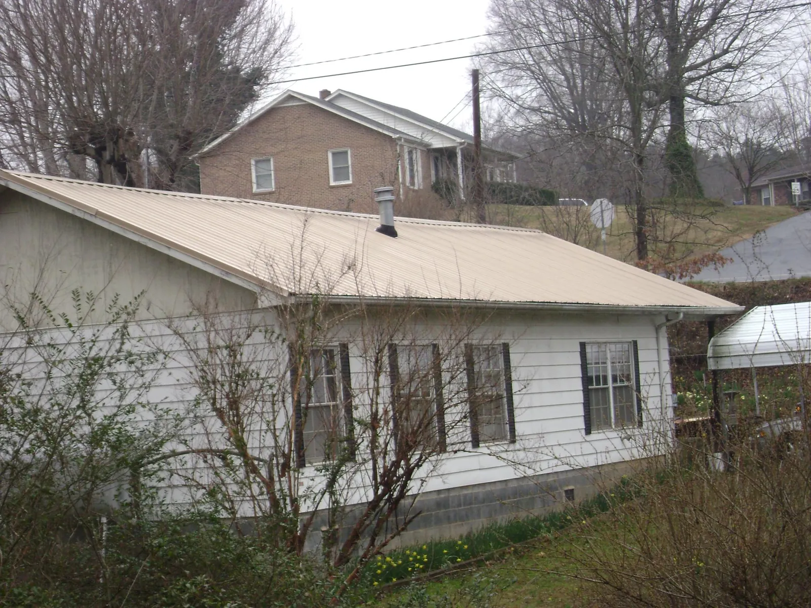 Tan metal roof on a white sided house set into a hillside — Commercial Roofing by Roofing Brothers in Cygnet